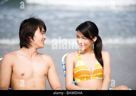 Coppia giovane seduto in sedie a sdraio sulla spiaggia guardando ogni altro Foto Stock