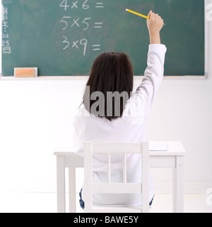 Ragazza in aula con mano sollevata vista posteriore Foto Stock