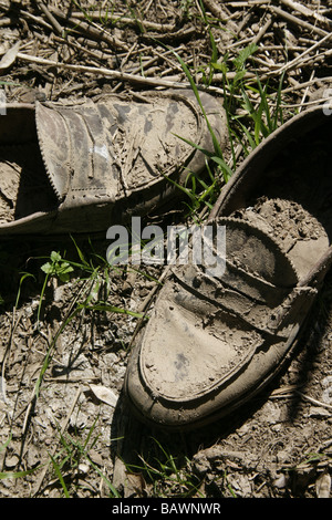 Un paio di scarpe marrone ricoperte di fango nel campo Foto Stock