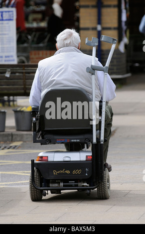 Uomo alla guida di uno scooter di mobilità con sue stampelle memorizzati sulla parte posteriore Foto Stock