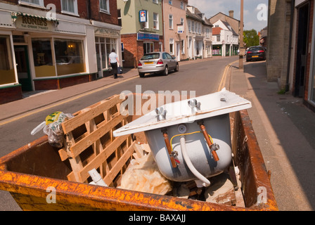 Un cassonetto situato nella strada in una città del regno unito riempito di rifiuti di cantiere comprendente una vecchia vasca da bagno Foto Stock