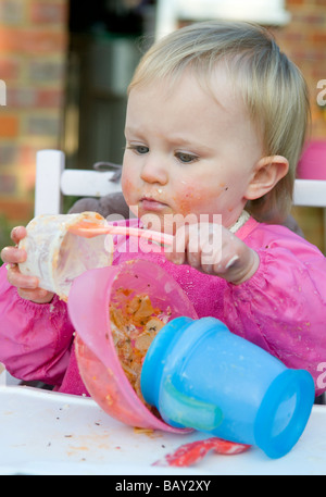 Il Toddler, 16mesi ragazza , alimentazione di se stessa e provocando un pasticcio Foto Stock