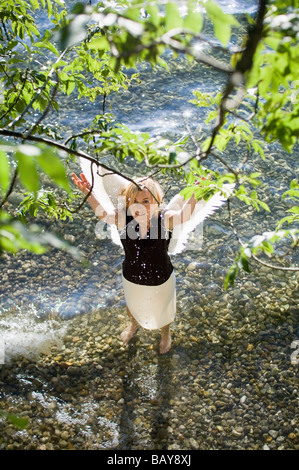 Metà donna adulta indossando ali d'angelo in piedi nel lago di Starnberg la spruzzatura di acqua, Baviera, Germania Foto Stock