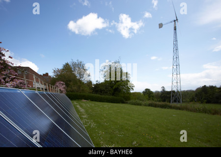 Sole che splende in giù su un array di tinta blu fotovoltaico in silicio policristallino pannelli solari e medie turbine eoliche Foto Stock