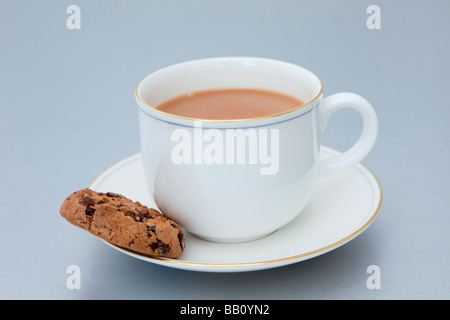 Una tazza di tè inglese e un piatto con un biscotto al cioccolato su uno sfondo semplice. Inghilterra Gran Bretagna Foto Stock