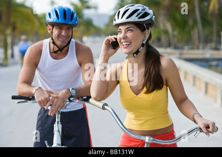 Donna ispanica sulla bicicletta parlando al cellulare mentre attende il fidanzato Foto Stock