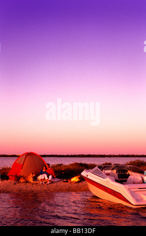 Giovane sulla riva con tenda e fuoco dopo la nautica con imbarcazione a motore per rilassarsi Foto Stock