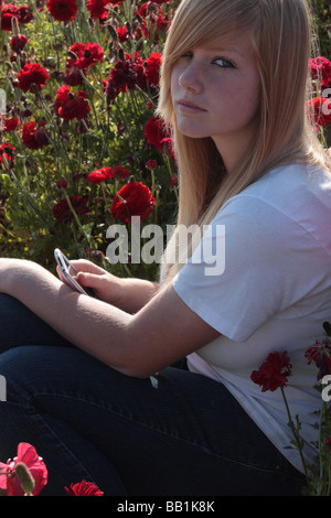 USA un ritratto di una bella ragazza adolescente di guardare direttamente la fotocamera e seduto in un campo di fiori di colore rosso Foto Stock