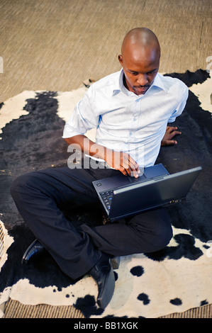 Imprenditore lavora su un computer portatile mentre è seduto su un Nguni pelle di mucca, per fortuna. Pretoria, Sud Africa Foto Stock