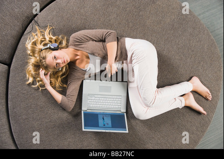 Donna sdraiata su un divano rotondo e ascolto di musica Foto Stock