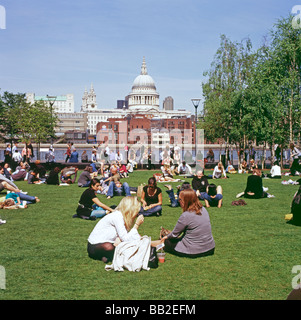 Persone rilassante al sole sul prato al di fuori della galleria d'arte Tate Modern vista della Cattedrale di St Paul sulla skyline di Londra UK KATHY DEWITT Foto Stock