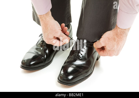 Primo piano di un mans mani come egli lega il suo nuovissimo vestono scarpe isolato su bianco Foto Stock