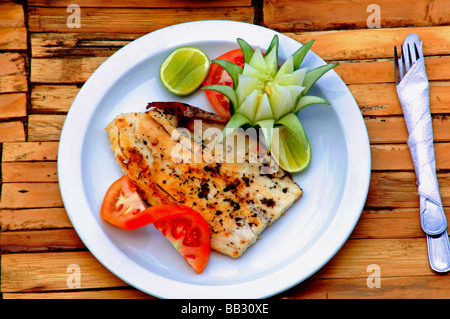 Piatto di deliziosa cucina sana contenente pesci tropicali frutta e verdure servita all'aperto su un rustico tavolo di bambù Foto Stock