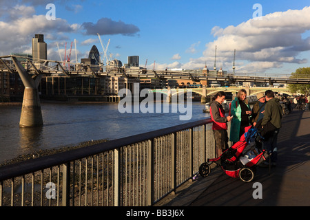 Una famiglia con un puschair talk in bassa luce del sole serale sulla banca del sud vicino al Millenium Bridge London REGNO UNITO Foto Stock