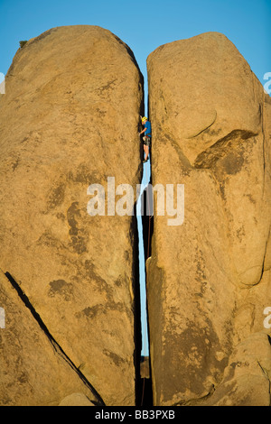 Scalatore spreme il suo modo il gap in una frazione di pilastro a Joshua Tree National Park California in un pomeriggio soleggiato Foto Stock