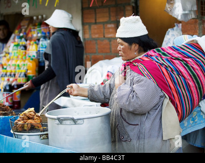 Un venditore ambulante a La Paz, in Bolivia si prepara un pollo mentre si sta portando il suo neonato sulla sua schiena. Vendita di alimenti e bevande Foto Stock