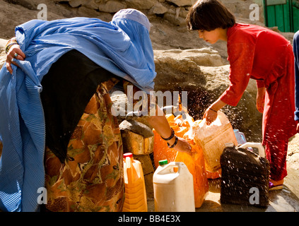 Donna in burqa e un bambino raccogliere acqua da un rubinetto locale a Kabul. Foto Stock