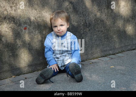 Triste ragazza seduta di fronte a un muro grigio Foto Stock