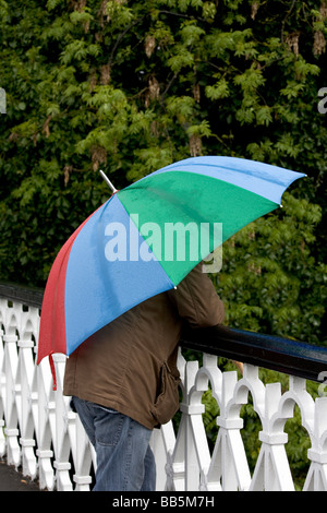 Uomo in piedi sul ponte sotto la pioggia con ombrello multicolore Foto Stock