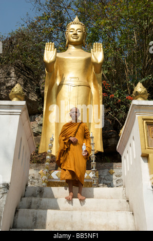 Un monaco buddista sta in piedi di fronte ad una statua di Buddha sulla scalinata che conduce fino a Phou Si hill al di sopra di Luang Prabang Laos Foto Stock