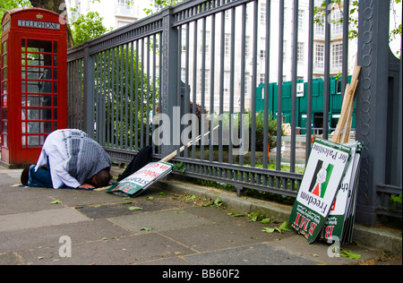 Prima di iniziare una protesta circa la situazione in corso nella Striscia di Gaza un uomo musulmano prega alla Mecca su una strada di Londra. Foto Stock