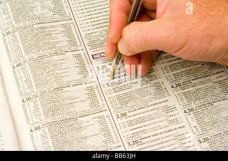 Man mano con una penna facendo una selezione di cavalli in un giornale Foto Stock