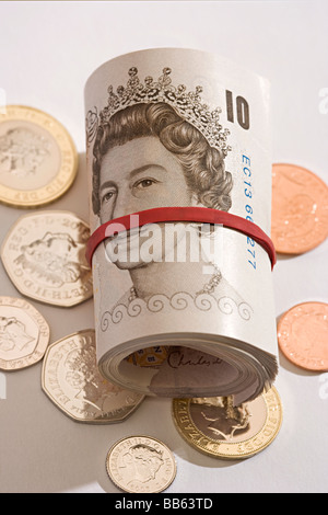 Nuovo e inutilizzato rotolo di sterline inglesi mint dieci pound banconote arrotolate giacente su di coniare monete inutilizzate. Foto Stock