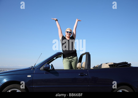 Giovane donna in autovettura convertibile in piedi con le braccia alzate Foto Stock