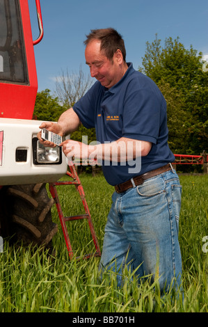 Agricoltore in piedi di fronte ad un irroratore Bateman utilizzando una calcolatrice per lavorare fuori spryaing tariffe Foto Stock