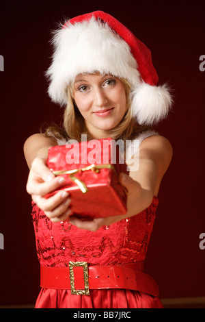 Donna sorridente, 20, indossando un Berretto di Babbo Natale e tenendo un presente, ritratto Foto Stock