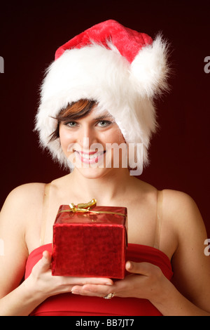 Donna sorridente, 23, indossando un Berretto di Babbo Natale e tenendo un presente, ritratto Foto Stock