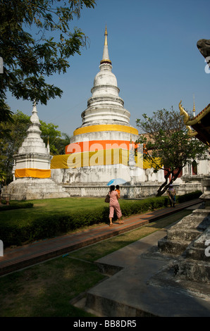 Una donna tailandese passa due zafferano pietra drappeggiato chedis del parco di Wat Phra Singh in Chiang Mai Thailandia Foto Stock