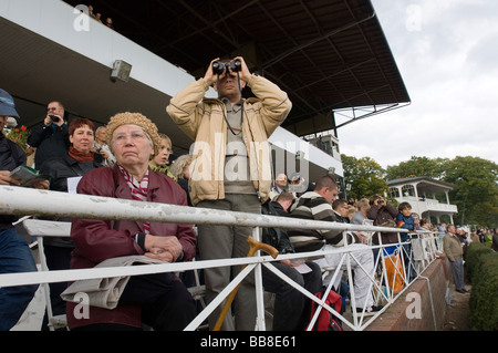 Gli spettatori a seguito di un cavallo di razza da una tribuna, alcuni con il binocolo, Berlino, Germania, Europa Foto Stock