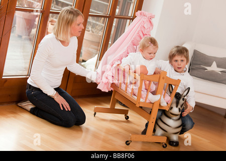 Madre di due bambini di 1 e 6 anni di OLS, giocano con una bambola della PRAM e un animale la pallina che rimbalza Foto Stock