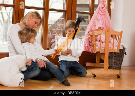 Madre seduta con i suoi due figli sul pavimento, 3 e 6 anni e la riproduzione Foto Stock