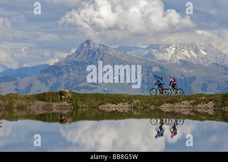 Gli amanti della mountain bike, maschio e femmina, riflettendo nel serbatoio dell'acqua Salvensee a Hohe Salve mountains, Tirolo, Austria Foto Stock