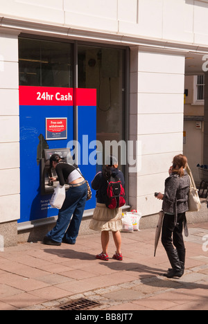 Persone queing fino a ritirare il denaro dalla Tesco bancomat foro nella parete speedbank atm in Norwich, Norfolk, Regno Unito Foto Stock