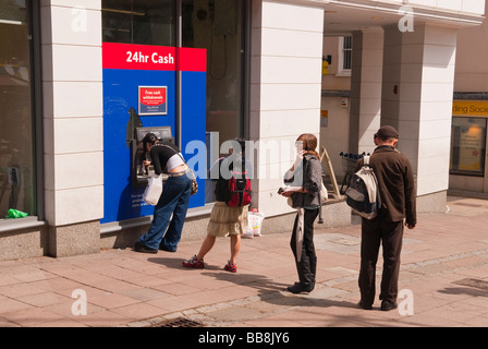 Persone queing fino a ritirare il denaro dalla Tesco bancomat foro nella parete speedbank atm in Norwich, Norfolk, Regno Unito Foto Stock