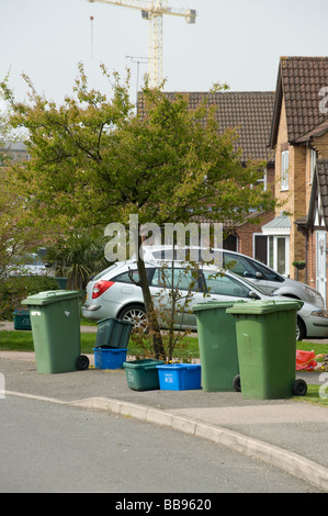 Fila di green wheelie bin contenenti i rifiuti di plastica e scatole di riciclo in una strada in attesa per la raccolta Foto Stock