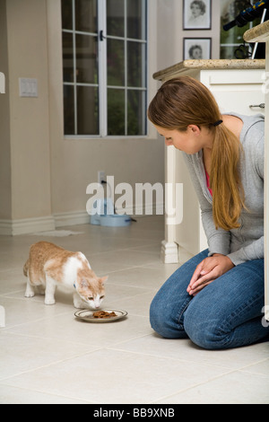 Alimentazione gatto pet ragazza adolescente 14-15 16-17 anni vecchio inginocchiato si inginocchia su pianale alimenta cat in cucina Signor © Myrleen Pearson Foto Stock