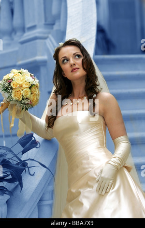 Basso angolo vista della bellissima giovane sposa con bouquet di fiori sfondo blu Foto Stock