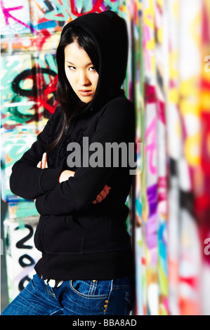 Giovane ragazza asiatica in rapper pongono di fronte a un muro con graffiti Foto Stock