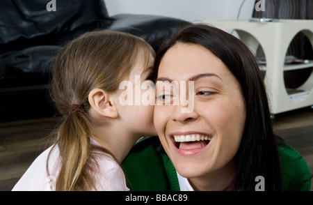 Una figlia sussurra a sua madre orecchio Foto Stock