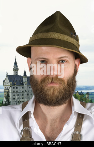Un uomo che indossa un cappello alpino e lederhosen con lo sfondo del castello di Neuschwanstein Foto Stock