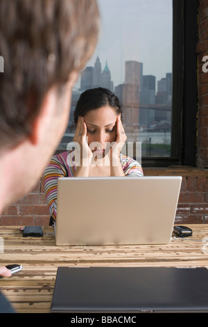 Donna seduta al computer portatile alla ricerca ha sottolineato Foto Stock