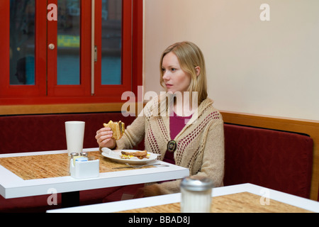 Una giovane donna seduta in un caffè e mangiare un panino tostato Foto Stock