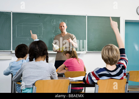 Vista posteriore di un gli studenti ad alzare la mano in una classe Foto Stock