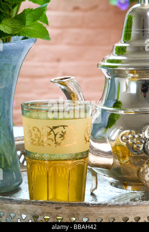 Il tè alla menta in un vetro dorato su un vassoio d'argento, con una teiera in argento e un vaso di foglie di menta fresca Foto Stock