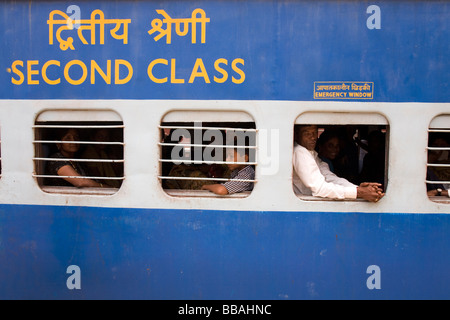 Persone sedersi all'interno di una seconda classe carrello di un treno in India. Molte delle finestre hanno barre su di essi. Foto Stock