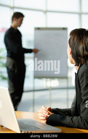 Executive femmina seduto alla scrivania, volgendo lo sguardo al collega in piedi accanto alla scheda Capovolgi Foto Stock